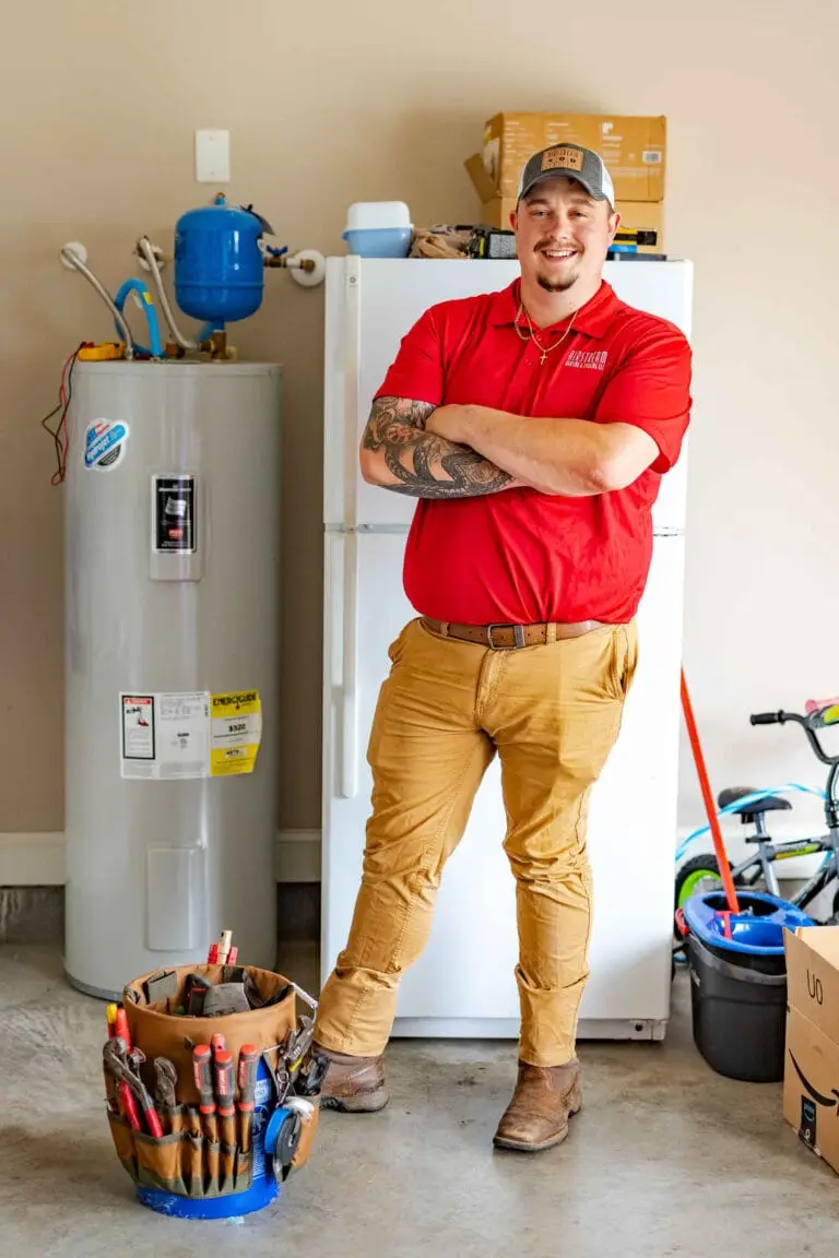 Airstream Services technician standing confidently beside a traditional tank-style water heater in a Middle Tennessee garage.