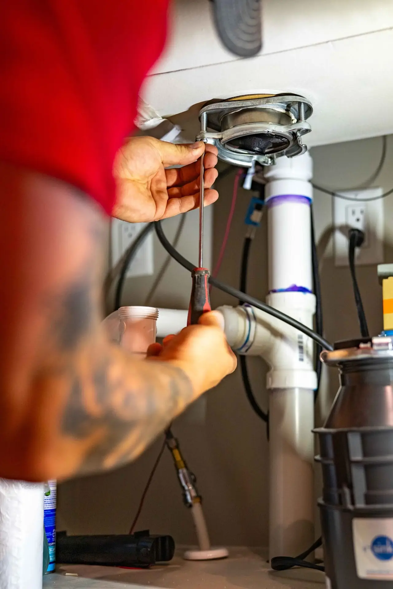 Airstream Services plumber using a screwdriver to work on drain components beneath a kitchen sink in a Middle Tennessee home.