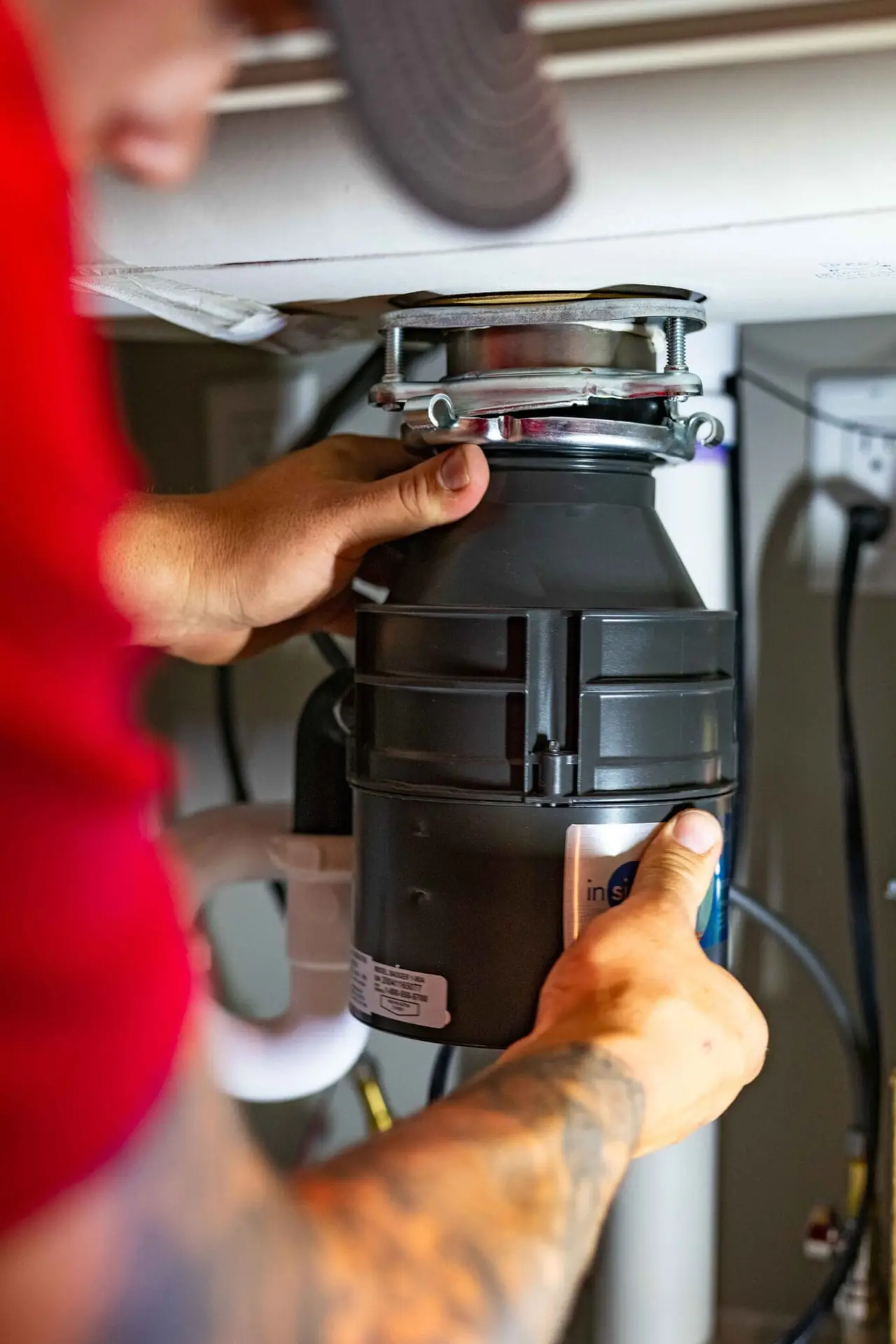 Airstream Services plumber installing or servicing a garbage disposal unit under a kitchen sink during a drain cleaning service.