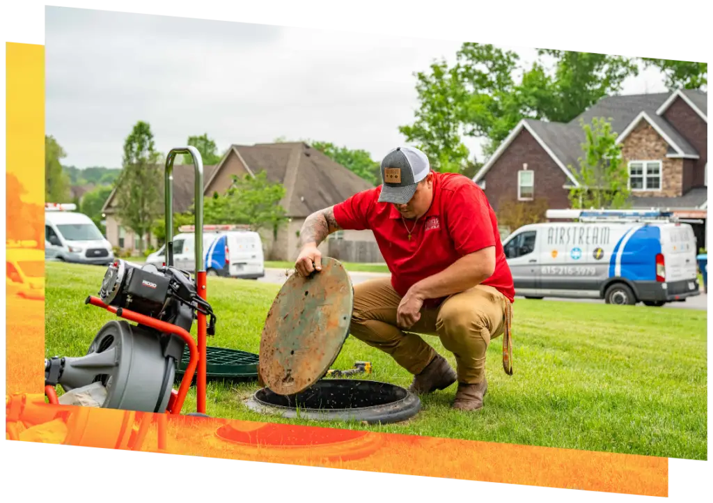 Airstream Plumbing, Heating & Air technician lifting a sewer cleanout cover with a drain cleaning machine nearby and branded vans in the background.