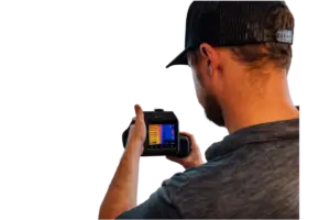 Technician from behind, wearing a cap and holding a thermal imaging camera with a colorful display.
